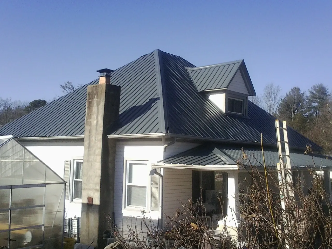 Dark blue standing seam metal roof on a white farmhouse with dormer — Slate & Tile Roof Repair by Roofing Brothers in La Crosse
